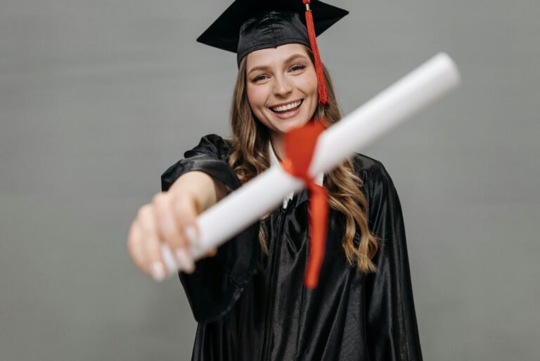 Happy female graduate wearing a cap and gown proudly holding her diploma with a smile.