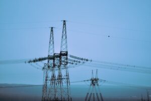 High voltage power pylons transmitting electricity under a clear blue sky in an open landscape.